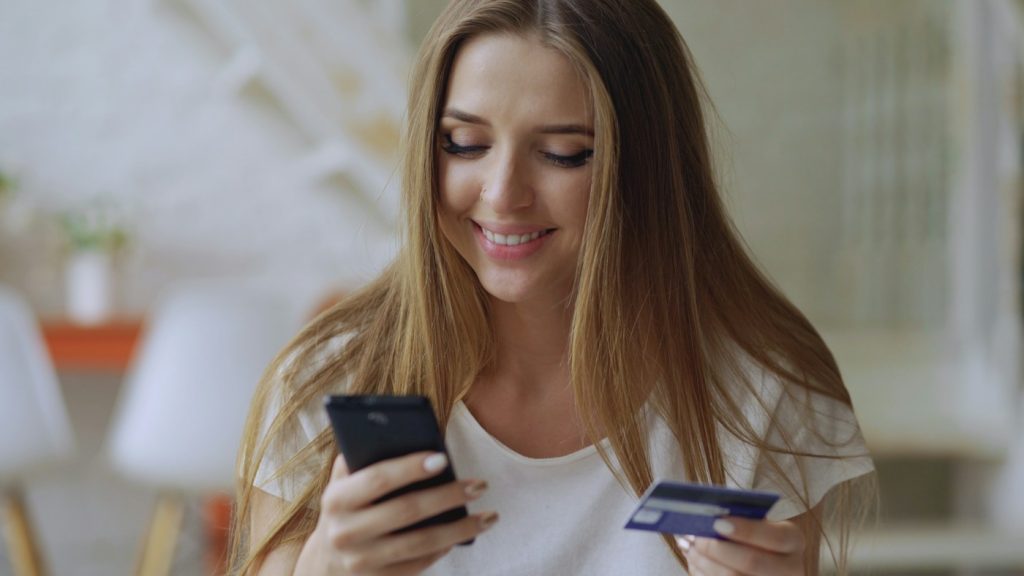 Elinde telefon ve banka kartı tutan gülümseyen bir kadın