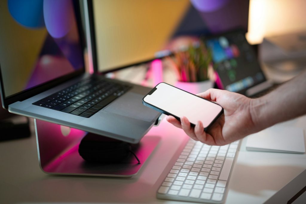 Dizüstü bilgisayarın önünde telefon tutan bir kişi